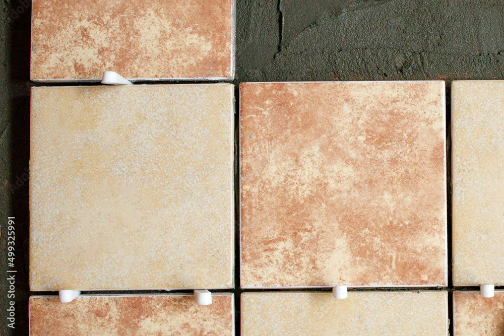 Fototapeta premium A section of freshly laid brown and cream tiles on the wall with plastic gaskets. Repair work