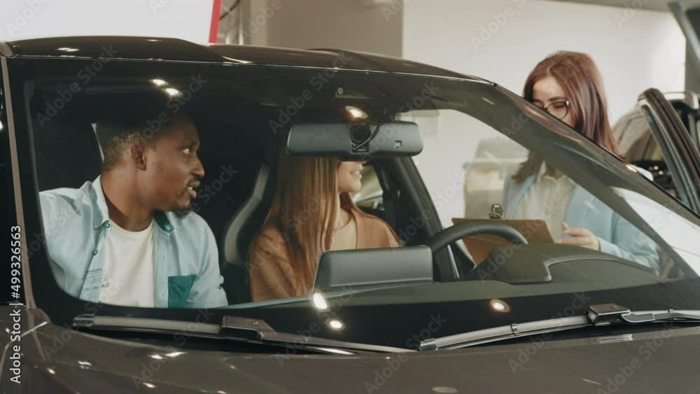 Female seller working with multiracial couple at modern auto center. Happy african man and caucasian woman consulting with manager while choosing new vehicle. Multi ethnic couple and saleswoman.
