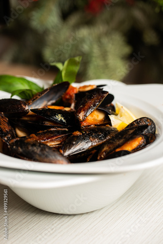Freshly cooked Seafood Shellfish mussels with cream, wine, cheese sauce and lemon in a white bowl, close-up, studio shot. A classic dish in Belgium, France and Netherlands. Restaurant food.