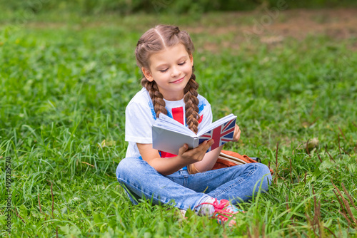 a teenager is studying an English language book on a green lawn in the warm season.