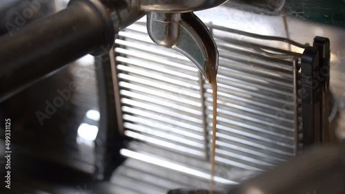 Freshly brewed coffee flowing out of a coffee machine and into a cup. The liquid is dark brown at first, then becomes lighter and creamier until it is very watery. photo