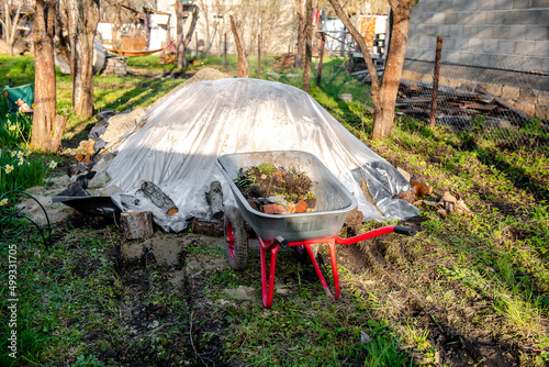 A wheelbarrow full of earth and stones in a garden plot. The concept of cleaning the garden plot in spring
