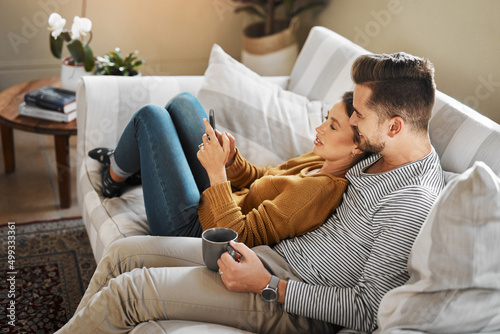 Lets see what shows are trending on social media. Shot of a young couple using a cellphone while relaxing on the sofa at home.