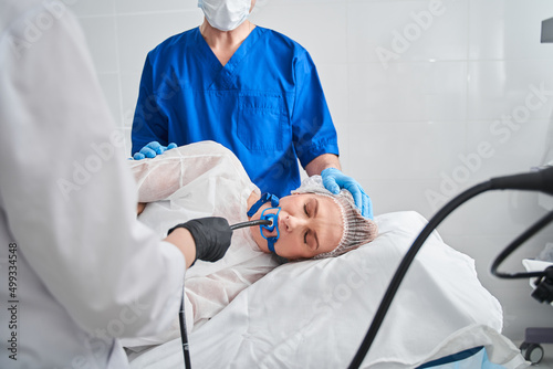 Woman laying at the bed while assistant holding special equipment at her mouth