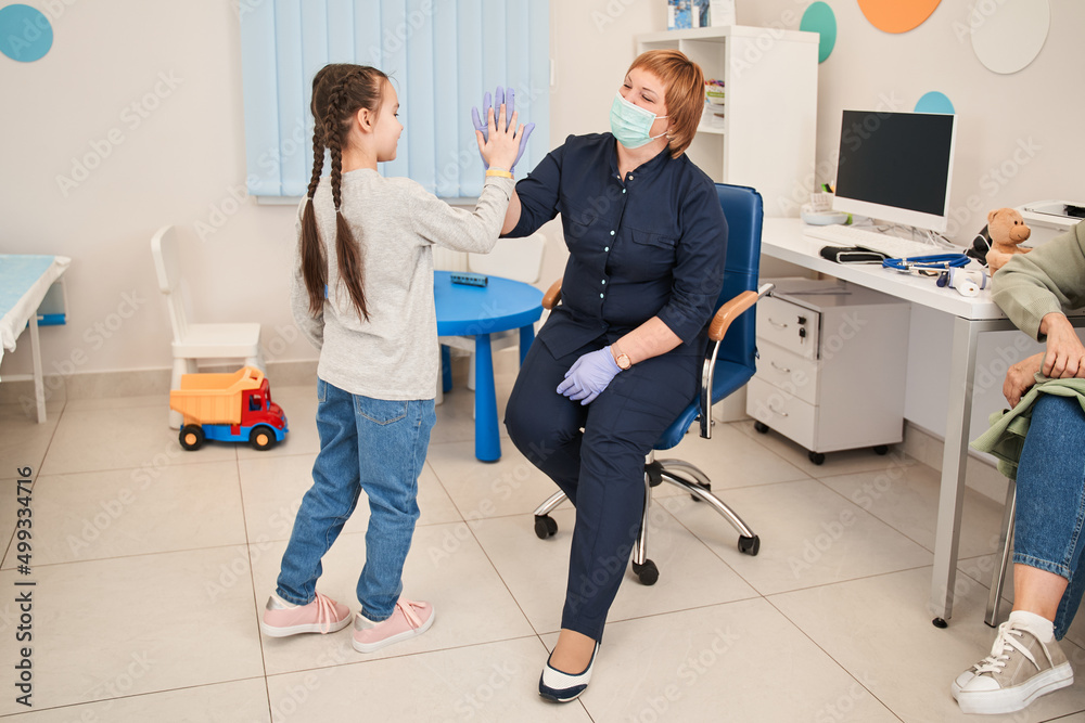 Smiling small patient celebrating successful treatment finish with general practitioner at checkup Smiling small patient celebrating successful treatment finish with general practitioner at checkup