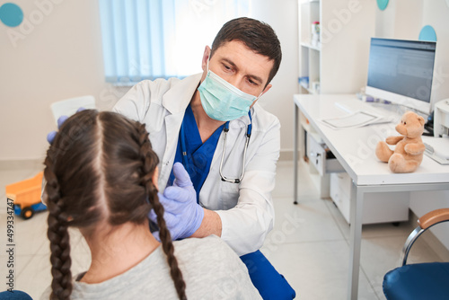 Caucasian doctor palpating school girl throat at clinic, sick daughter visiting pediatrician