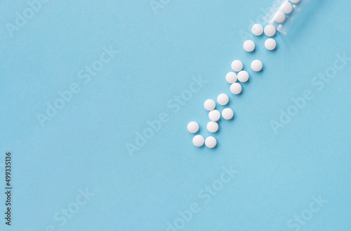 Different white pills and a plastic container on a blue background. Medical theme. 