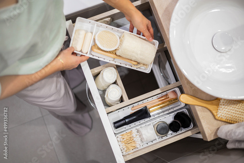 Top view of woman hands neatly organizing bathroom amenities and toiletries in drawer in bathroom.