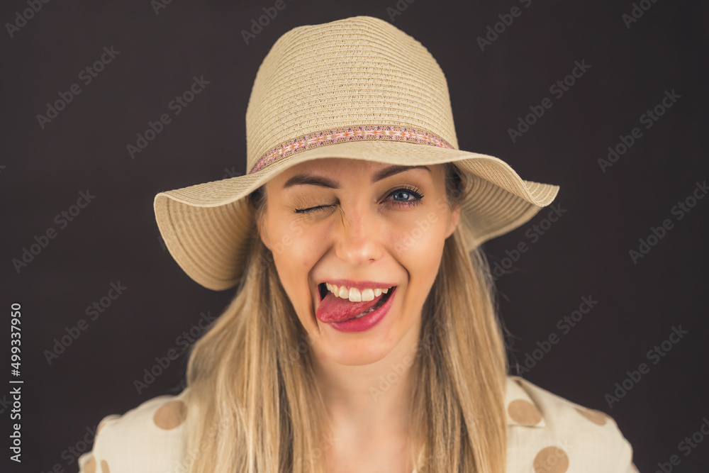 Portrait of a young beautiful caucasian blonde woman in studio, sticking out tongue, wearing beige hat over black or dark-gray background. High quality photo Portrait of a young beautiful caucasian blonde woman in studio, sticking out tongue, wearing beige hat over black or dark-gray background. High quality photo