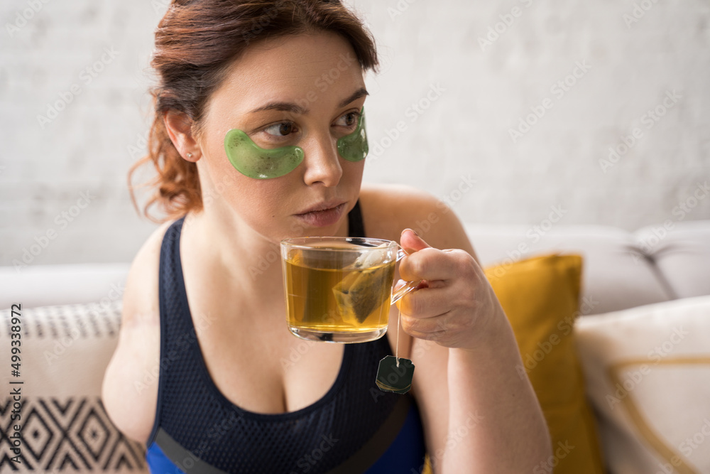 Woman without arm drinking tea and looking away while relaxing at her living room Woman without arm drinking tea and looking away while relaxing at her living room