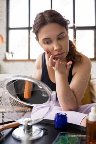 Caucasian woman looking at her skin attentively while taking care of her face
