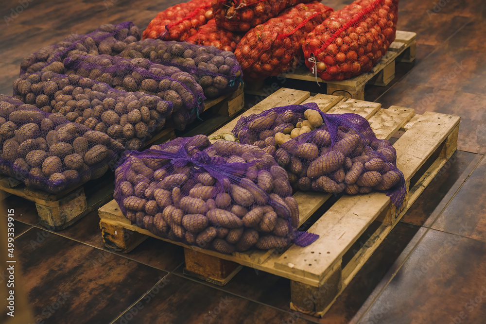 Φωτογραφία Fresh raw potatoes and onions in mesh bags on pallets in grocery department of f