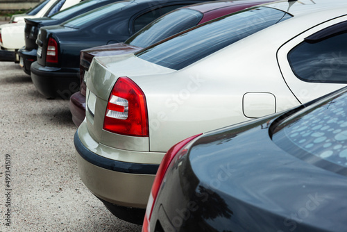 The back of the trunk is visible in the parking space on blurred background. Transportation and parking. Row of cars and vans parked in parking lot during the daytime.
