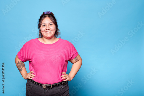 Young curvy latina woman smiling looking at camera isolated on blue background. Copy space.