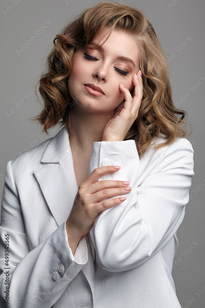 Portrait of young woman in casual white jacket with eyes closed and hand near face.