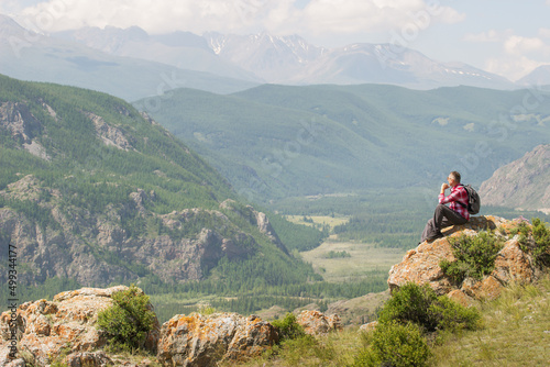 Active man hiker sitting on top rock looking at panorama in sunny summer morning on mountain outdoor. The concept of tourism travel and male loneliness.