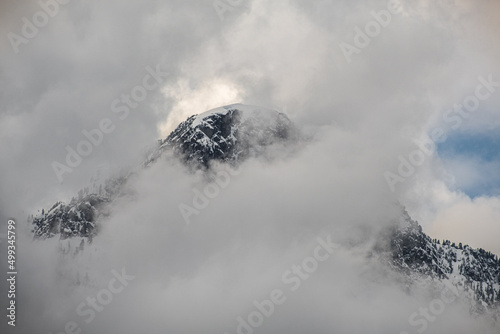 Clouds and fog shroud snow covered mountains and the mountain forests