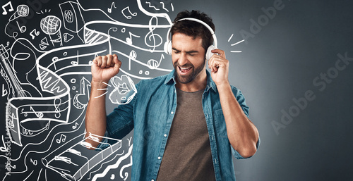 Jamming out to the music. Studio shot of a handsome young man listening to music while standing beside illustrations against a grey background.