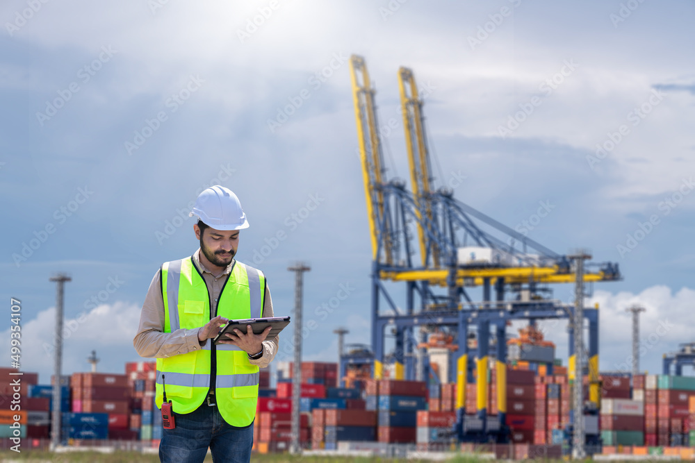 Engineer wearing uniform inspection and see detail on tablet with logistics container dock cargo yard with working crane bridge in shipyard with transport logistic import export background. Engineer wearing uniform inspection and see detail on tablet with logistics container dock cargo yard with working crane bridge in shipyard with transport logistic import export background.