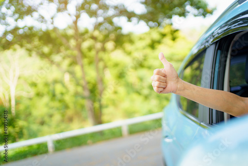 Unrecognizable Asian woman driver showing a thumb up outside the vehicle while driving a car. 