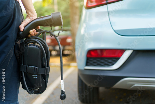 Unrecognizable woman holding the portable EV emergency charging adapter and preparing to charge the EV car. 