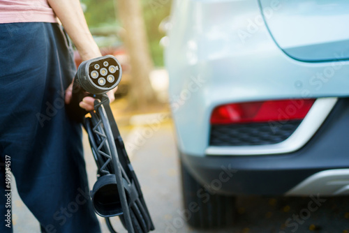 Unrecognizable woman holding the portable EV emergency charging adapter and preparing to charge the EV car. 