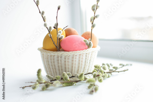 Colored Easter eggs in a white basket, medium on a white background. In the basket are flowers willow. Holiday concept