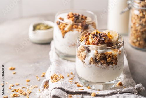 Crunchy granola with yogurt, banana, nuts, chocolate and honey in a glass on white background. Healthy breakfast concept.