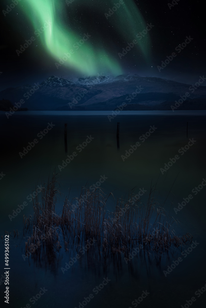 Epic vibrant Northern Lights Aurora composite image over landscape of Loch Lomond and mountains in Scotland