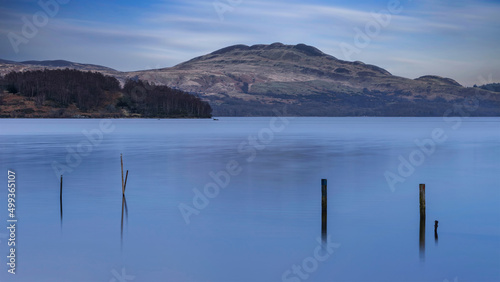 Beautiful landscape image of Loch Lomond and snowcapped mountain range in distance viewed from small village of Luss