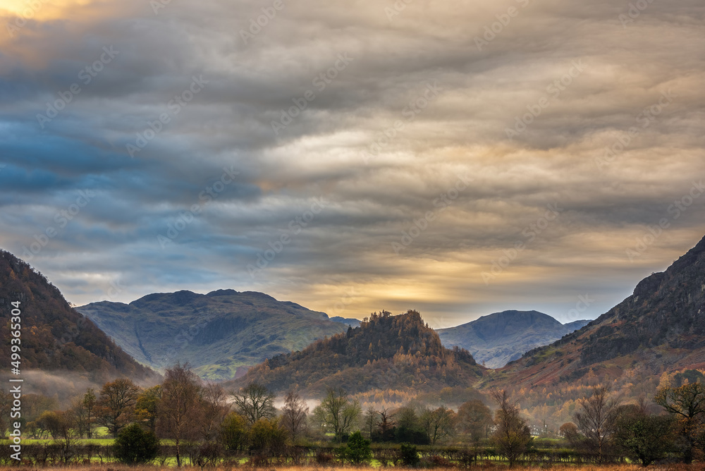 Stunning Autumn landscape sunrise image looking towards Borrowdale Valley from Manesty Park in Lake District with fog rolling across the landscape