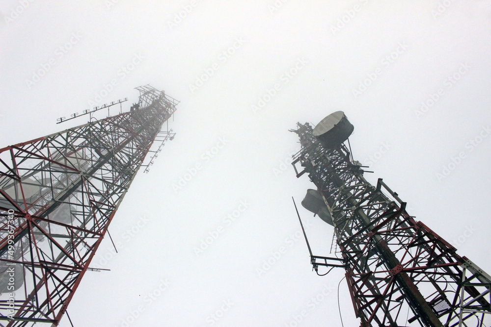 View looking up at two telecommunication masts tailing off into the mist. Microwave link and TV transmitter towers. No people. - obrazy, fototapety, plakaty 