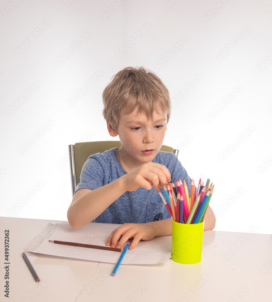 Cute little boy with blonde hair draws at a table, white background Cute little boy with blonde hair draws at a table, white background