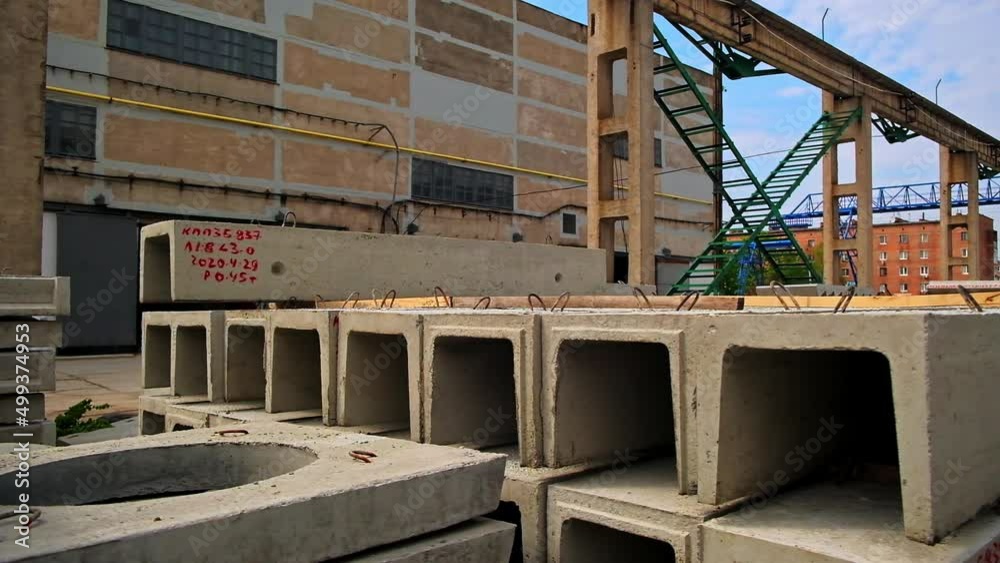 Long ferroconcrete beams with metal loops on top. Diverse building materials for construction outdoors. Old warehouse at backdrop.