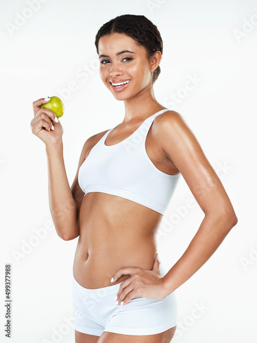 You know what they say about a apple a day. Portrait of an attractive young woman holding a apple in her hand while standing against a white background.