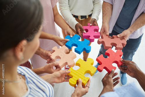 Diverse team of happy creative young multiracial people putting together colourful pieces of jigsaw puzzle. Cropped close up shot. Teamwork and problem solving concepts