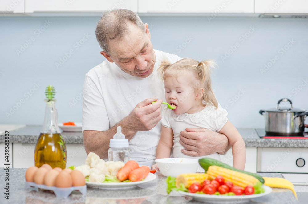 Grandfather feeding baby girl with a spoon at kitchen