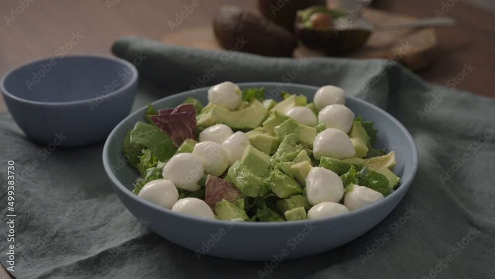 Man making salad with mixed greens avocado and mozzarella in blue bowl