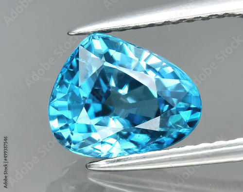 Natural gemstone blue zircon in tongs on a gray background photo