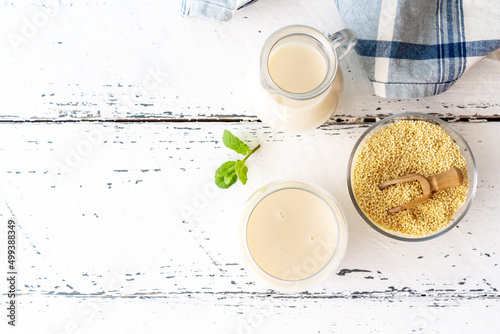 Millet milk in glass, jar and bowl on white wooden table with copy space photo