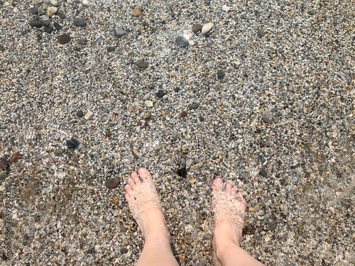beautiful feet of white woman standing in sea with small pebbles in summer