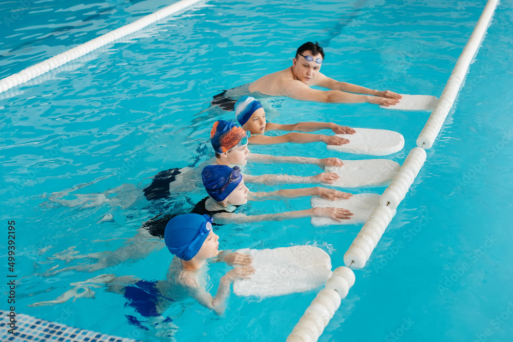 A group of boys and girls train and learn to swim in a modern swimming pool with an instructor. Development of children's sports. Healthy parenting and promotion of children's sports.