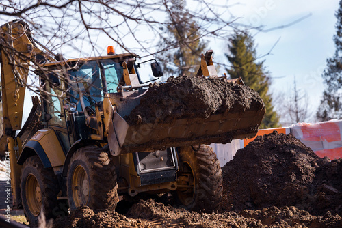 The excavator backfills the pit with the front bucket. Moves soil around the construction site. Heavy construction equipment