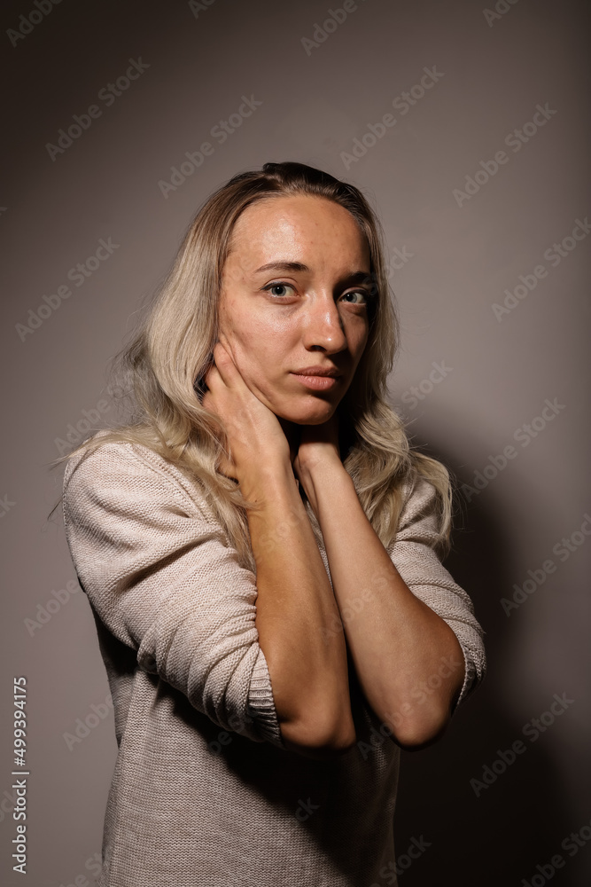 A young woman in grief with a sad face hugs her neck with her hands A young woman in grief with a sad face hugs her neck with her hands