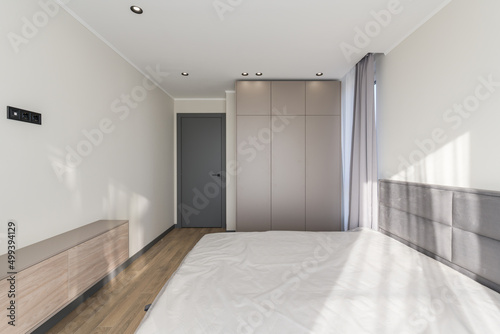 Empty room in a modern style with a large bed  light walls and a stylish gray wardrobe