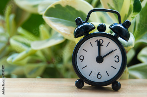 Black alarm clock isolated on blurred nature background. The clock set at 2 o'clock. Copy space concept photo