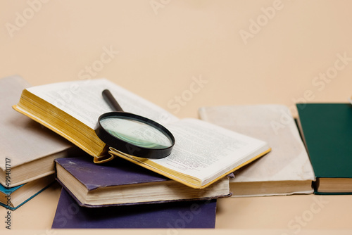 A stack of books with a magnifying glass highlighted on a beige background. Search for information. world book day.