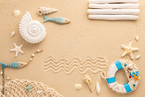 Summer concept. Sea frame with Ammonite, starfishes,snail shell, wooden fishes and lifebuoy on sand. Top view. Copy space.