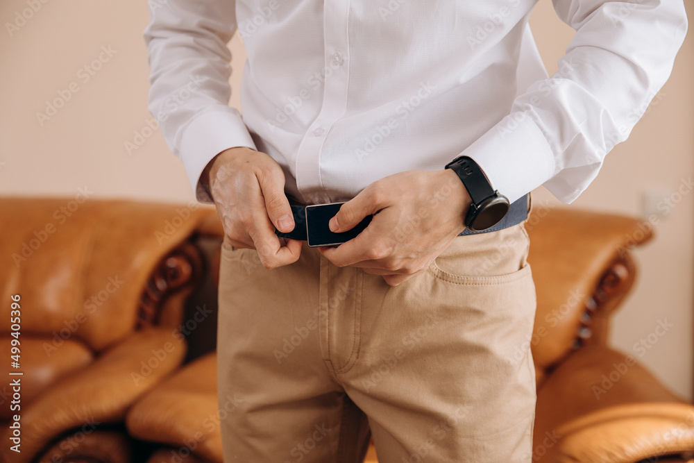 The groom holds out a belt on the wedding day