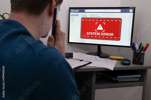 Office worker in front of computer with warning about system error on screen. A man is on the phone with IT support to solve a problem. Error Network Problem Technology Software Concept.